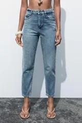 Pantalón de jean gris oscuro, de corte mom fit, tiro alto y largo tobillero. Cuenta con cinco bolsillos, cierre frontal con cremallera y botón.