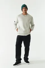 Buzo de felpa color gris claro, con cuello redondo, mangas largas y costuras a contratono. Presenta lettering estampado en el pecho, bolsillos laterales y logo en grifa de goma.