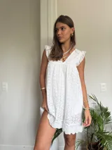 Vestido corto blanco de algodón con bordado tipo broderie anglaise, escote en V y mangas cortas con volado. Presenta un corte imperio con frunce bajo el busto.