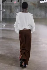 Blusa color marrón con escote en pico, manga larga abullonada con elástico en los puños y volantes en el escote y mangas.