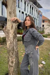 Chaqueta de jean gris con cuello clásico, cierre frontal con botones, dos bolsillos con solapa en el pecho y estampado de rosas con strass en el frente y la espalda.