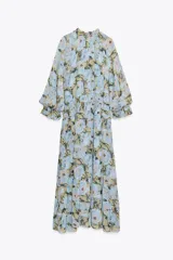 Vestido largo con estampado floral en tonos celeste, amarillo y marrón. Tiene cuello redondo con volantes y lazada, escote pico, manga larga con puño elástico con volantes, forro interior y cierre frontal con botones.