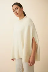Poncho color crema de tejido de punto industrial con cuello alto y aberturas laterales para los brazos.