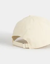 Gorra deportiva color crudo, de tela canvas con bordado frontal de la palabra "Wellness" en letras negras estilo universitario. Tiene visera curva y tira ajustable trasera con hebilla metálica.