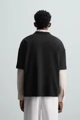 Camiseta negra de corte holgado, cuello redondo y manga corta. Estampado frontal con diseño abstracto en color blanco.