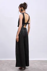 Pantalón negro de tiro alto, corte ancho y largo, con pliegues frontales y pespuntes contrastantes en blanco en la cintura y bolsillos.