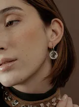 Par de aros colgantes con argollas doradas y dijes circulares de resina transparente con incrustaciones de strass de colores. El dije mide aproximadamente 1.5cm de diámetro.