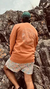 Buzo color ladrillo de corte estándar con cuello redondo y puños y cintura acanalados. Estampado en la espalda con diseño de una ola, un sol y una palmera.