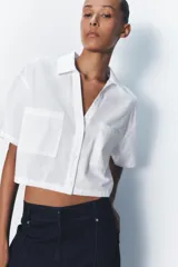 Camisa celeste de popelín con cuello solapa, escote pico y manga corta. Presenta dos bolsillos delanteros de parche y cierre frontal con botones.