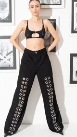 Pantalón de jean negro de corte oversize con argollas metálicas plateadas a lo largo de las piernas.