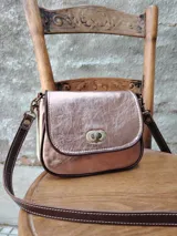 Cartera bandolera pequeña de cuero sintético color bronce con textura craquelada. Tiene correa larga de cuero marrón regulable y cierre metálico dorado.