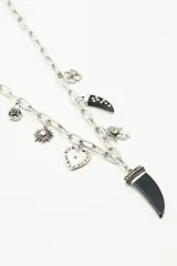 Collar largo con cadena gruesa plateada y dijes colgantes de diferentes formatos: mano de Fátima, corazón con strass, cuerno negro y cuentas de cristal.