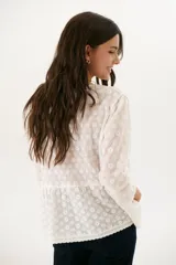 Camisa blanca con bordado floral, cuello en V y cierre frontal con botones.