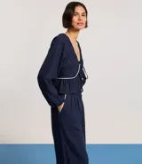 Blusa de mangas largas color azul marino, confeccionada en viscolino con 30% de lino, con escote V, lazo en el cuello con punta y bieses contrastantes luego abajo del escote, además del bajo de volado.