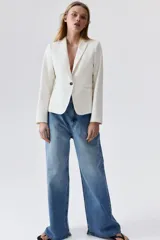 Blazer entallado color blanco, con solapas de muesca y cierre de un botón. Bolsillos de adelante ribeteados, botones decorativos en los puños y abertura atrás.