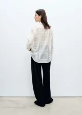 Camisa blanca con bordado de flores y detalles calados, de corte recto y manga larga con puños abotonados. Confeccionada en lyocell y poliéster.