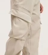 Pantalón cargo recto color beige, con cintura elástica ajustable con cordón, bolsillos laterales tipo cargo con solapa y bolsillos con cremallera.
