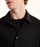 Camisa de manga larga color negro, con cuello inglés y abotonado frontal. Confeccionada en tejido piqué de poliamida y elastano, con tecnología performance que ofrece elasticidad, secado rápido y menor arrugado.