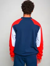 Sweater deportivo Umbro del Club Nacional de Football, con mangas raglán rojas y cuerpo azul marino. Presenta el logo de Umbro bordado en blanco y el escudo del club en el pecho. Detalles en blanco en los laterales.