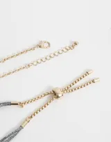 Set de dos pulseras doradas, una con cadena y dijes colgantes de strass con forma de trébol, corazón, rombo y flor. La otra pulsera es de hilo de lurex gris con cadena dorada y dijes de dados dorados.