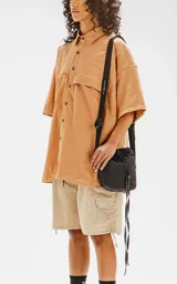 Camisa manga corta color beige, con cuello clásico, cierre frontal con botones, doble bolsillo con ojal en el delantero y silueta oversize.