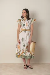 Vestido midi de algodón color natural con estampado de flores, hojas y aves en tonos verde, naranja y marrón. Tiene cuello mao, mangas cortas con volados y apliques de hilo, bolsillos laterales y cinturón de soga color beige.