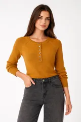 Sweater de tejido de punto color mostaza, de manga larga y calce holgado. Presenta cuello redondo con una pequeña abertura frontal abotonada con botones marrones.