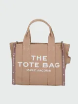Bolso tipo tote pequeño de Marc Jacobs confeccionado en tejido jacquard color tostado. Presenta el texto 'THE TOTE BAG MARC JACOBS' bordado en el frente en contraste, asas de mano superiores y cintas laterales con inscripciones de la marca.