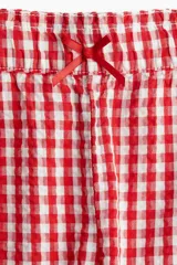 Short de algodón con estampado de cuadros vichy rojos y blancos, cintura elástica con moña de satén y ribete de volados en el bajo.