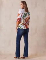 Buzo blanco con estampado abstracto en tonos naranja, verde, marrón y rojo. Tiene cuello redondo y mangas 3/4.