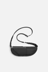 Bandolera negra de tela técnica con correa ajustable. Tiene un compartimento principal con cierre de cremallera, un bolsillo interior plano con cremallera y dos bolsillos frontales, uno de ellos con cremallera.
