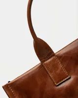 Cartera de mano verde militar en cuero liso, con asas cortas y correa ajustable.