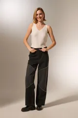 Pantalón de jean negro lavado, tiro alto, corte recto y ancho. Presenta paneles diagonales en la parte delantera de las piernas adornados con tachas metálicas plateadas.