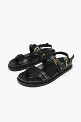 Sandalias planas de cuero negro con dos tiras horizontales sobre el empeine y una tira trasera ajustable con hebilla.