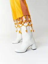 Botas de caña media de cuero sintético blanco con plataforma y tacón cuadrado. Presentan un detalle de cuentas de madera y cordón amarillo alrededor de la caña.