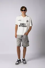 Remera tejida color crudo con cuello tipo chomba en V, mangas cortas con rayas negras y estampado con letras en el frente. Confeccionada en hilado de algodón.