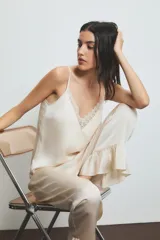 Conjunto de pijama color crema con detalles de encaje en el top. El top es de tirantes finos y el pantalón es largo con volados en el ruedo.