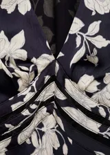 Vestido midi de mangas cortas con estampado floral blanco sobre fondo negro. Tiene escote en V con detalle de frunce en el centro del busto y falda con corte al bies.