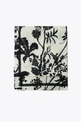 Pañuelo rectangular de color crema con estampado de ramas y flores en negro. Tiene terminaciones deshilachadas.