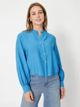 Camisa celeste de corte cropped, sin cuello, con mangas largas abullonadas y puños con botón.