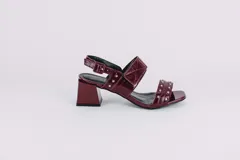 Sandalias de cuero charol color borgoña con taco cuadrado y plataforma. Presentan dos tiras anchas sobre el empeine con apliques metálicos redondos y tira trasera con hebilla.