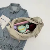 Cartera tipo hobo de tela suave color verde oliva, con correa ajustable al hombro y dos bolsillos frontales con detalle de trenzado.