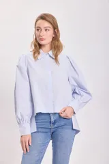 Camisa celeste a rayas verticales, con cuello clásico, cierre frontal con botones, mangas largas abullonadas y corte asimétrico.