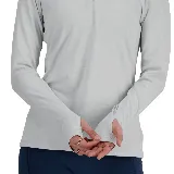 Camiseta deportiva New Balance color gris claro jaspeado, de manga larga con orificios para los pulgares, cuello alto con cierre de cremallera corto y logo reflectante en el pecho.