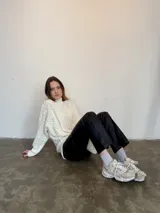 Sweater tejido en lana italiana con alpaca y viscosa, color crudo, con cuello alto y mangas largas. Diseño con trenzas en el frente y mangas. Corte holgado.