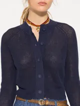 Cardigan azul marino de tejido de lino y algodón, largo hasta la primera cadera. Tiene mangas largas con puños acampanados de tela plana y cierre frontal con botones.