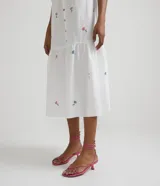 Vestido camisero midi blanco con estampado de flores rosas y celestes, manga corta abullonada, cuello camisero, abotonado al frente y falda con volantes.