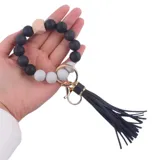 Llavero pulsera con cuentas redondas de silicona en colores blanco y negro, un cubo de madera natural, borla de cuero sintético negra y gancho metálico dorado.