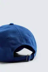 Gorra azul con visera confeccionada en tejido de algodón y parche frontal con texto bordado en blanco. Ajuste en la parte posterior.