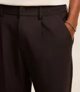 Pantalón de vestir marrón oscuro, de corte loose, con pliegues, bolsillos laterales y traseros.